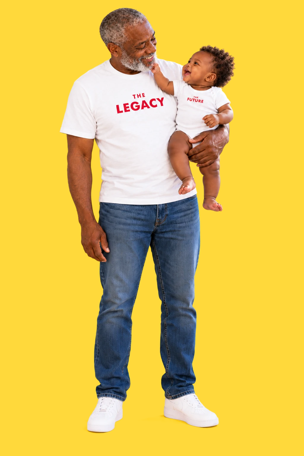 A smiling grandfather holds a laughing baby against a yellow background. His white T-shirt reads THE LEGACY, and the baby's white onesie reads THE FUTURE.
