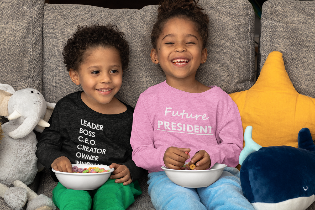 Two kids laughing on a couch in Fearlessly Hue® tees that read Leader, Boss, C.E.O. and Future President