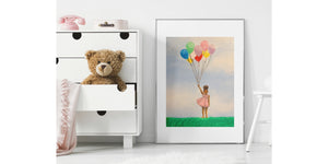 Girl with balloons matted print in a silver frame leaning against the wall of a girl's bedroom with a teddy bear peeking out of the dresser drawer third from the bottom.
